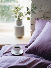 Fototapeta na wymiar cup of coffee and flowers. Cup of coffee on the bed. flower on the windowsill. sunlight in the bedroom