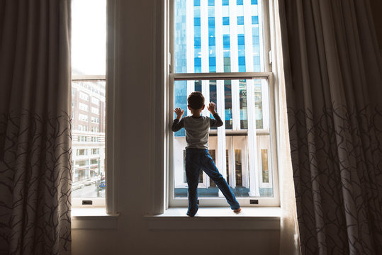 A Sihouette Of A Boy Standing In Front Of A Window In The Middle Of A City