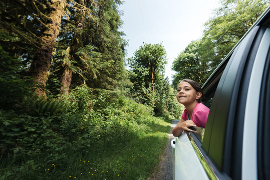 A young girl leans out of a white car window on a beautiful day