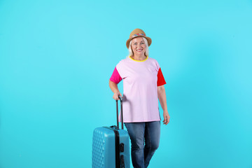 Senior woman with suitcase on color background. Vacation travel