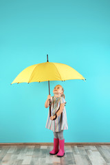 Little girl with yellow umbrella near color wall