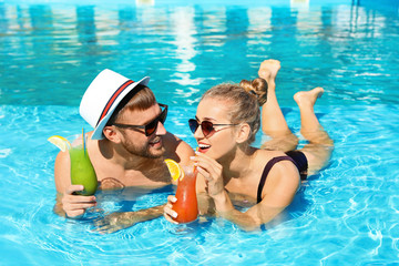 Naklejka premium Young couple with refreshing cocktails in swimming pool at resort