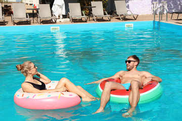 Happy young couple with inflatable rings in swimming pool
