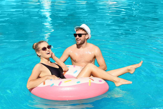 Happy young couple with inflatable ring in swimming pool
