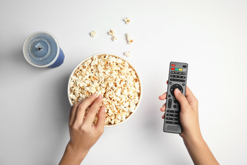Woman with TV remote eating popcorn on white background, top view. Watching cinema