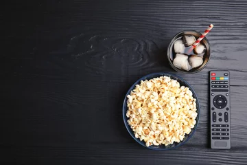 Rolgordijnen Bowl with popcorn, glass of iced cola and TV remote on wooden background, top view with space for text. Watching cinema © New Africa