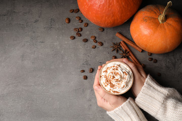 Woman holding cup of tasty pumpkin spice latte on gray table, flat lay with space for text