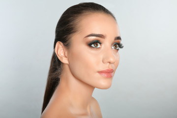 Fototapeta premium Portrait of young woman with eyelash extensions and beautiful makeup on light background