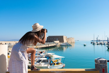 Elegant young tourist visitor woman walking on a sightseeing tour at Heraklion Venetian port, Crete, Greece. Venetian fort at background. - obrazy, fototapety, plakaty