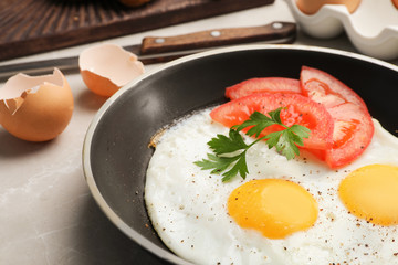 Pan with fried sunny side up eggs and tomato on table, closeup
