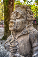 Fototapeta na wymiar Stone statue of a dwarf. Marble sculpture of fairy gnome in Salzburg Mirabellgarten park, Salzburg, Austria