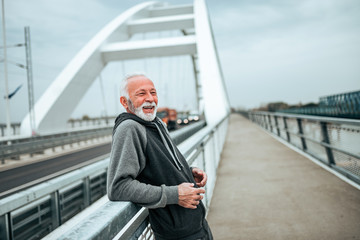 Smiling senior sportsman relaxing on the bridge on the city.