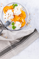 Sliced persimmon with yogurt and almonds. Healthy food concept on light background. top view