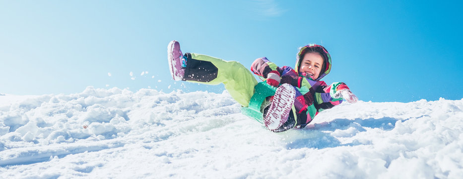 Little Happy girl slides down from the snow slope with blue sky background