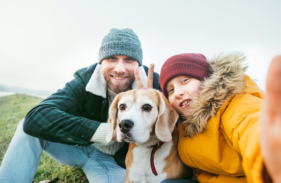 Father and son dressed in warm clothes taking a selfie photo with their best family member beagle dog.