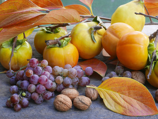 persimmons, grapes,  quince and walnuts on a rustic wooden table with leaves, full frame