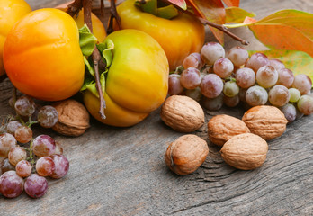 persimmons, grapes,   and walnuts on a rustic wooden table with leaves and copy space
