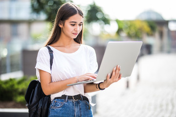 Young charming girl working with a laptop standing somewhere in the city.