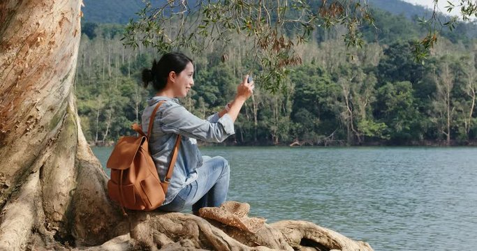 Woman take photo on cellphone and sit on the old tree root in forest