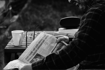 Closeup of lonely old Man reading newspaper and book with drinking tea or coffee in home back garden