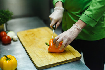 cook in gloves cuts vegetables on a wooden board. professional kitchen with steel worktop