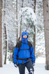 Determined young male mountain climber hiking through deep powder snow in fir tree forest. Wearing heavy backpack with camping equipment. Active lifestyle in cold weather.