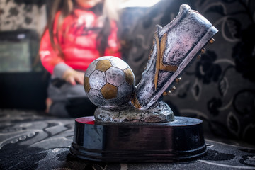 Closeup of gray metal football soccer winning trophy with little girl that has achieved it