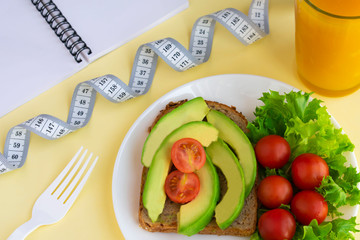 Healthy vegetarian snack with avocado, cherry tomatoes, lettuce leaves, glass of juice, measuring tape. Top view. Diet or weight control concept.