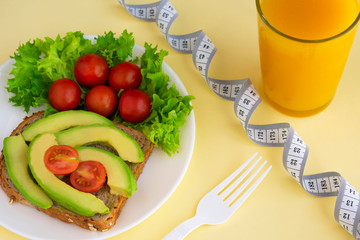 Healthy vegetarian snack with avocado, cherry tomatoes, lettuce leaves, glass of juice, measuring tape. Top view. Diet or weight control concept.