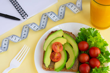 Healthy vegetarian snack with avocado, cherry tomatoes, lettuce leaves, glass of juice, measuring tape. Top view. Diet or weight control concept.