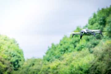 Black camera drone in flying with visible propellers movement in a green field at springtime