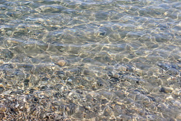 Crystal clear sea water surface seabed visible texture clean ripples abstract background pebbles shallow beach