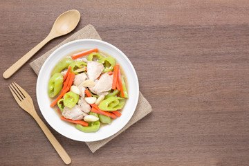 top view of stir fried chicken with banana pepper in a ceramic dish on wooden table. hot and spicy homemade style food concept.