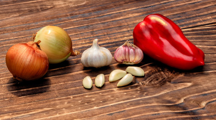 close up on garlic, red bell peppers and onions over dark wood