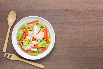 top view of stir fried chicken with banana pepper in a ceramic dish on wooden table. hot and spicy homemade style food concept.