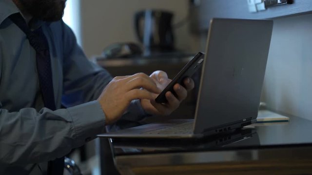 Young businessman comparing data on laptop and smartphone by table in office
