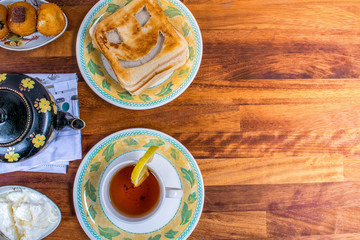 Closeup of top View of Fresh morning breakfast with , teapot, tea, funny face toast, cake, yogurt, magazine on yellow wooden table , dairy products.