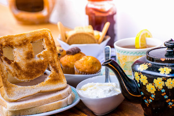 Closeup of Fresh morning breakfast with , teapot, tea, funny face toast, cake, yogurt, biscuits and magazine on a brown wooden table , dairy products.