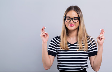 Young woman crossing her fingers and wishing for good luck on a gray background