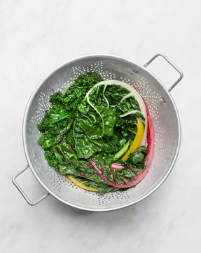 Red and yellow steamed chard drains in a colander. 
