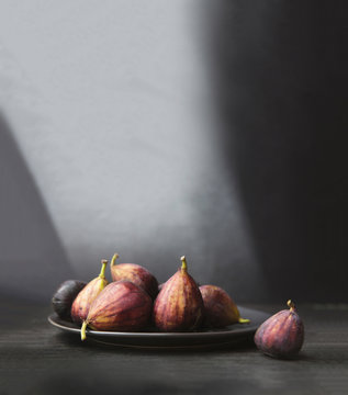 Figs are bathed in a stream of light on a gray surface.