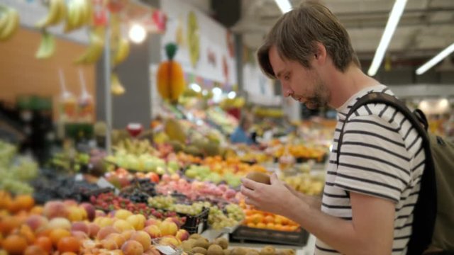 Hard choosing between red and green apples in grocery market. Young caucasian man make his choice in fruit section of supermarket vegetables. Comparing of two different goods