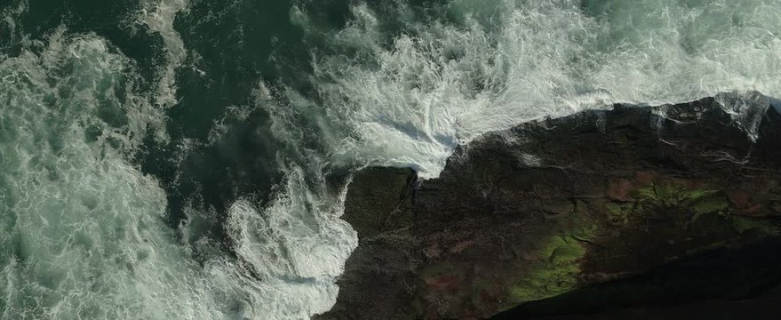 Wave hits rocks with algae from birds eye drone