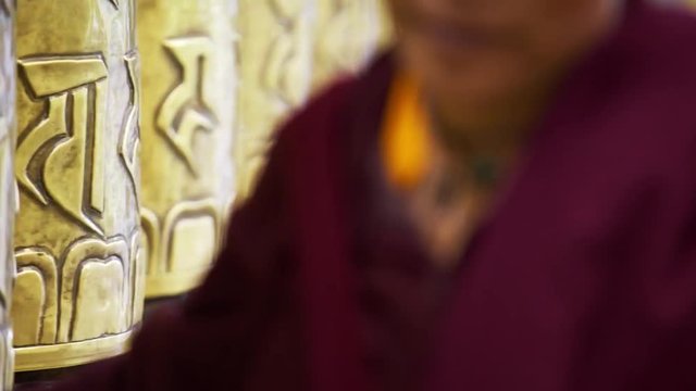 Unrecognizable buddhist monk touching and rotating metal prayer wheels in Macleod Ganj residence of Dalai Lama