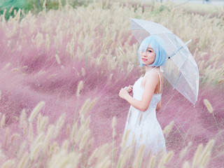 Portrait of beautiful young Chinese woman wearing white halter dress, holding transparent umbrella, smiling in pink hairawn muhly flowers fields. Emotions, people, beauty and lifestyle concept.
