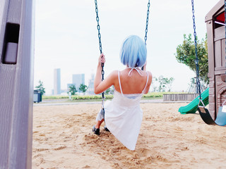 Rear view of beautiful young Chinese woman wearing white halter dress sitting on swing and looking...
