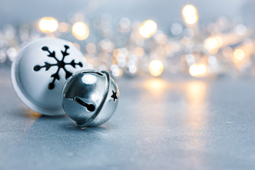 festive christmas jingle bells on grey background with blurred garland lights. macro view