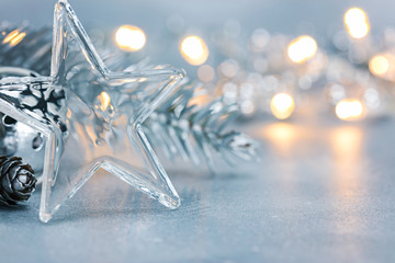 transparent glass star with christmas jingle bell and fir tree branch on blurred silver background...