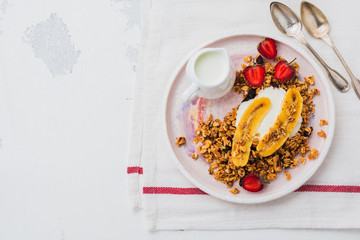Oatmeal granola with yoghurt, fresh strawberries and banana, chia seeds, sunflower and honey in white ceramic plate on light background. Top view.
