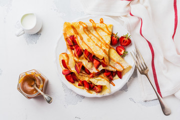 Сrepes with fresh strawberries and caramel on light concrete old table background. Top view.